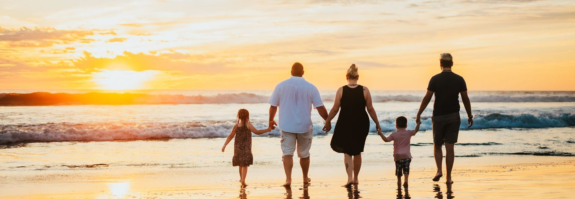 A family is walking on the beach at sunset holding hands.