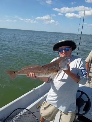 Man on boat holding large redfish, ocean backdrop.