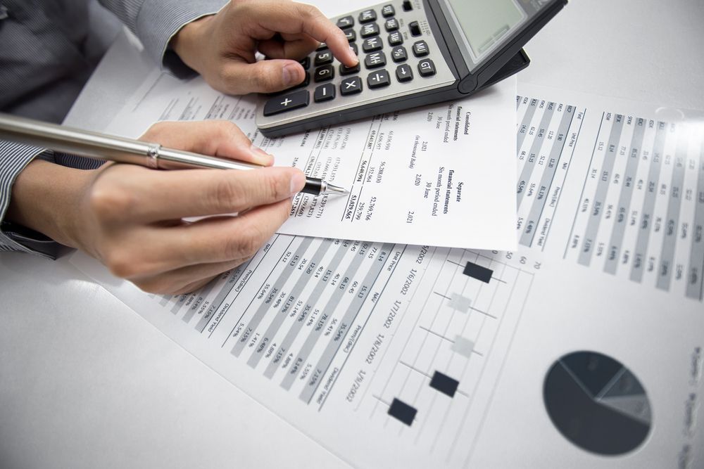 Hands with pen and calculator reviewing financial charts and paperwork on a desk