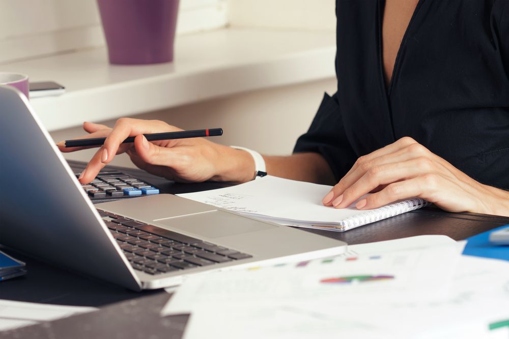 Woman Using Calculator and Laptop at Desk, Taking Notes — Careful Books in Mareeba, QLD