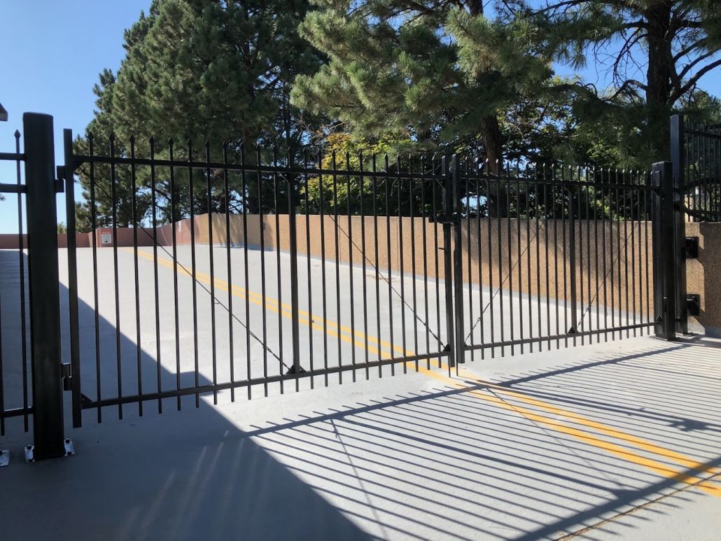 A black metal fence is surrounding a parking lot with trees in the background.