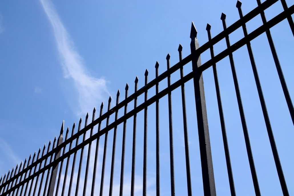 A close up of a wrought iron fence against a blue sky.