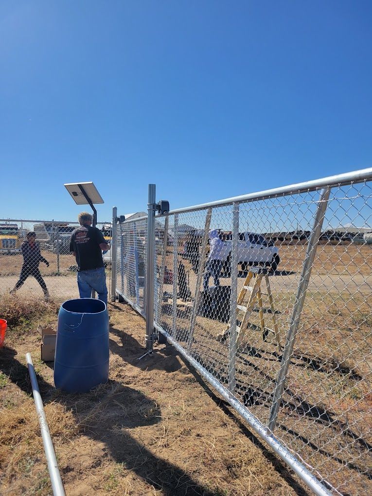A man is working on a chain link fence in a field.