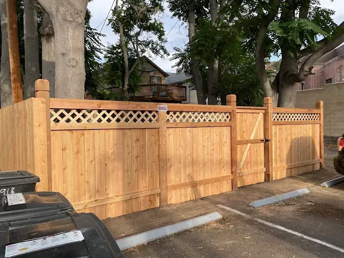 A wooden fence with a gate is in a parking lot.