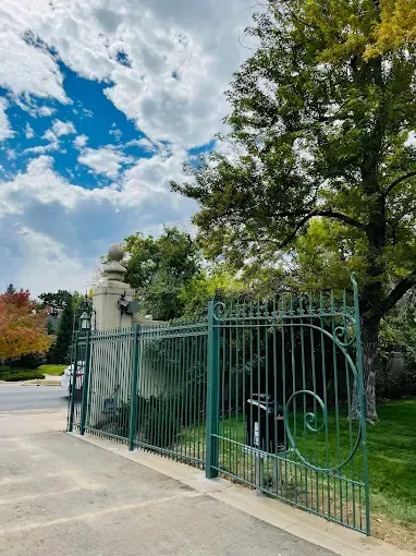A green wrought iron gate is surrounded by trees and grass.