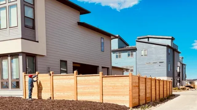 A man is standing next to a wooden fence in front of a house.