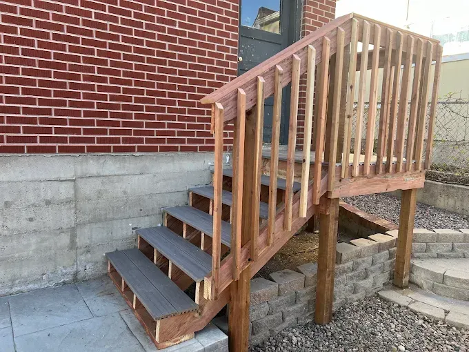 A wooden deck with stairs leading up to a brick building.