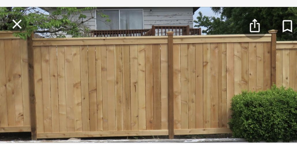 A wooden fence with a bush in front of it and a house in the background.