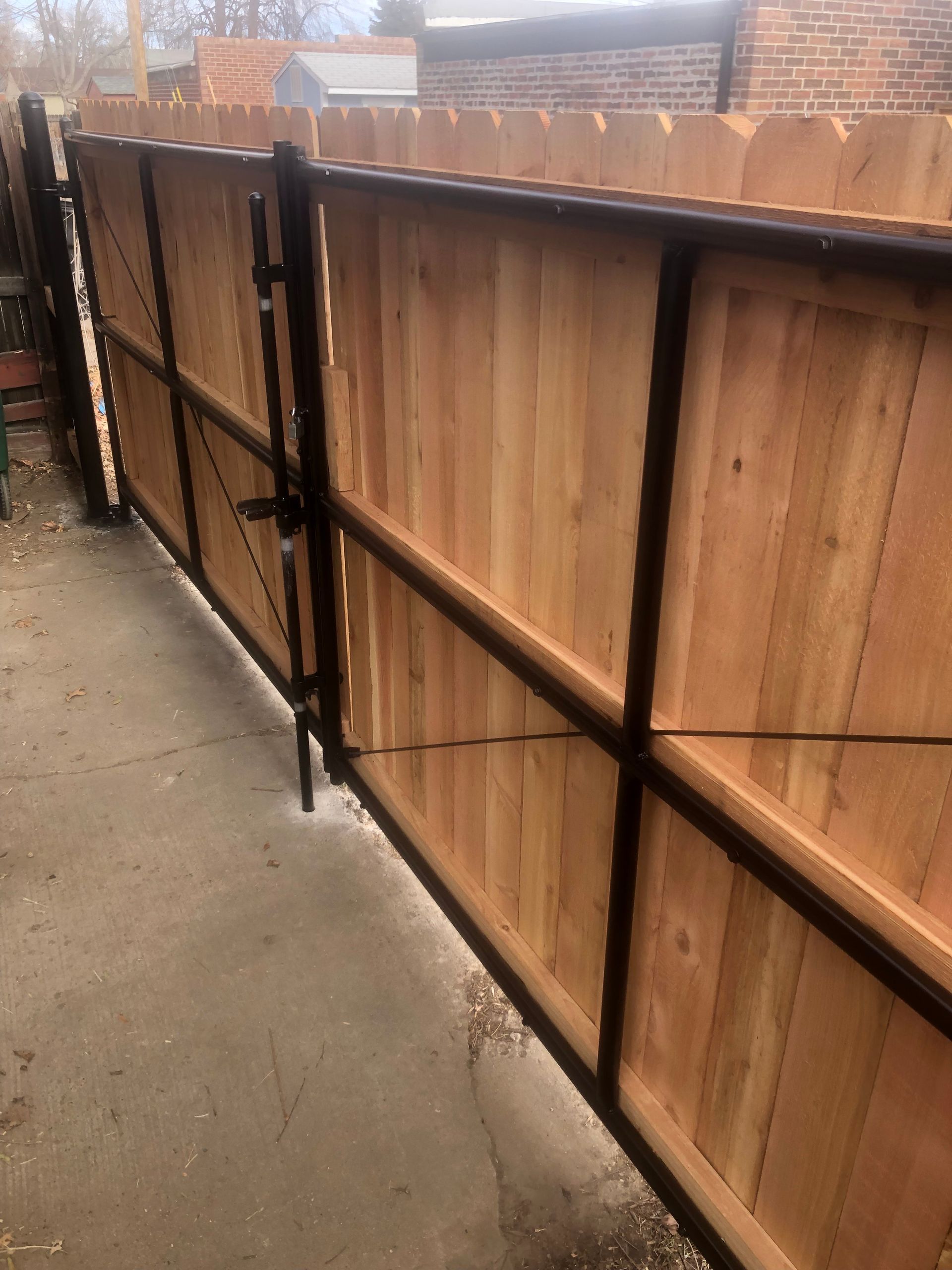 Wooden fence with black metal frame and gate on a concrete surface.