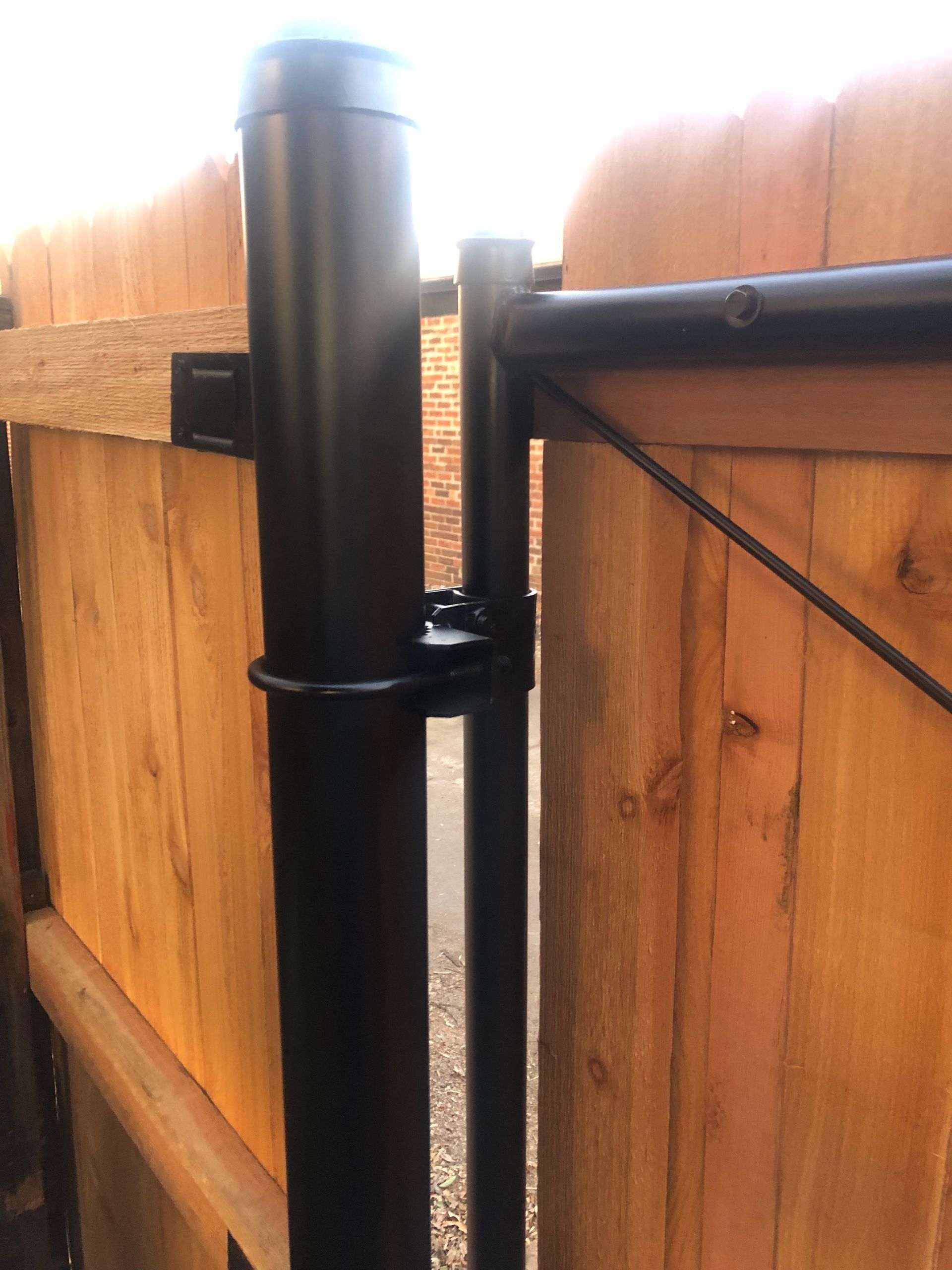 Black metal gate hinge on a wooden fence post, outdoors.