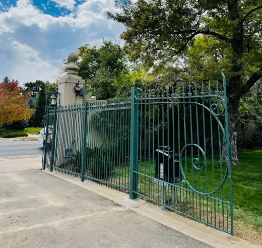 A green wrought iron gate is surrounded by trees and grass.