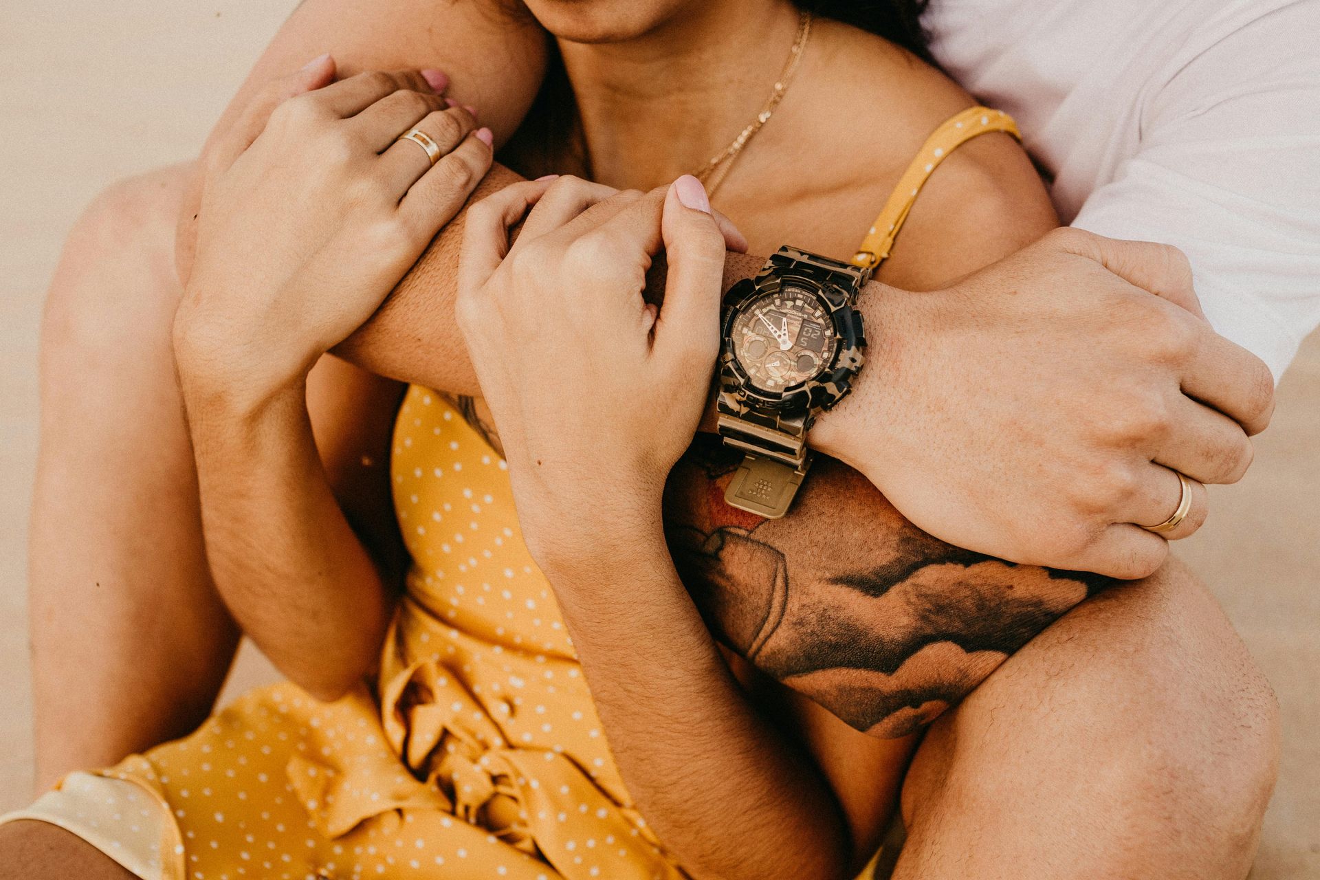 Couple embracing, arms wrapped around each other. Woman in yellow dress, man wearing watch.
