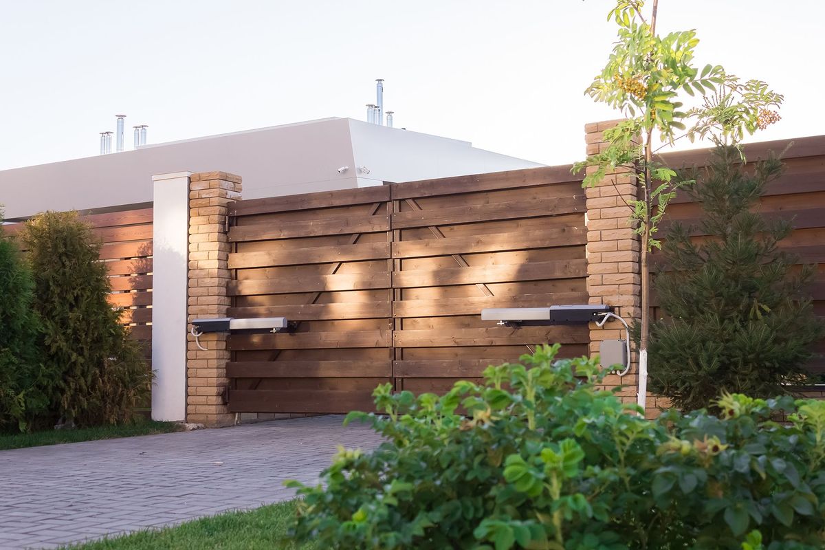 A wooden gate with a brick pillar is surrounded by trees and bushes.