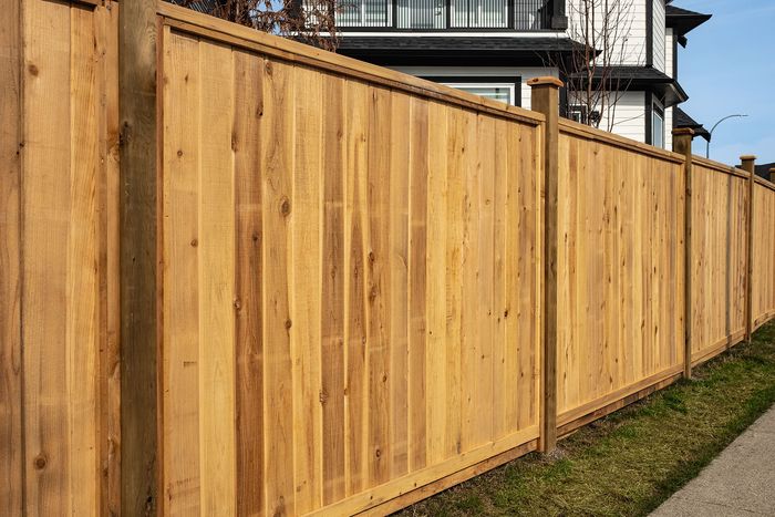 A wooden fence is sitting next to a sidewalk in front of a house.