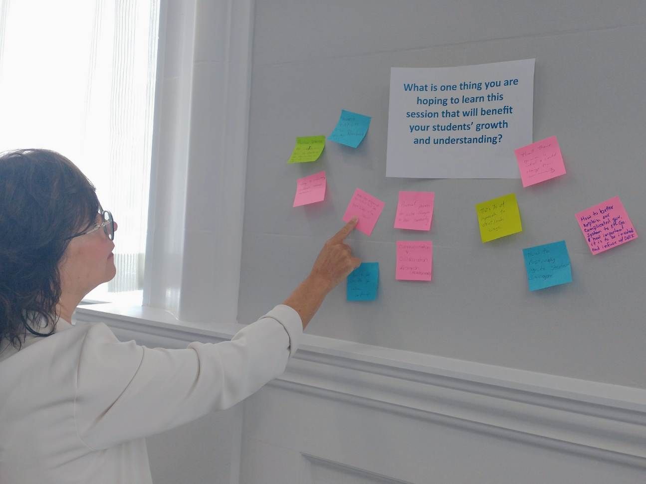 A woman is pointing at sticky notes on a wall.