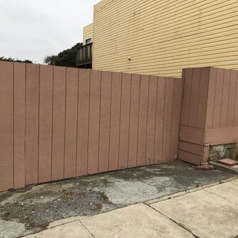 A wooden fence is sitting next to a sidewalk in front of a building.