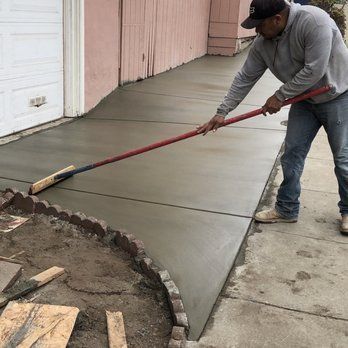 A man is using a broom to spread concrete on a sidewalk.