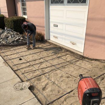 A man is working on a concrete driveway in front of a garage door.