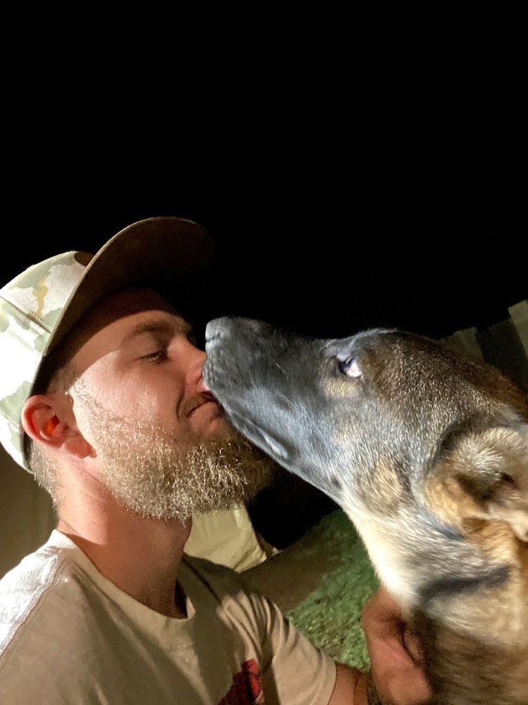 A man with a beard is kissing a dog on the nose.