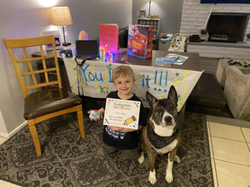 A boy is sitting on the floor next to a dog holding a certificate.