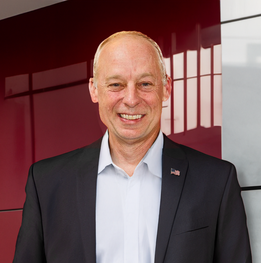 A man in a suit and white shirt is smiling in front of a red wall.