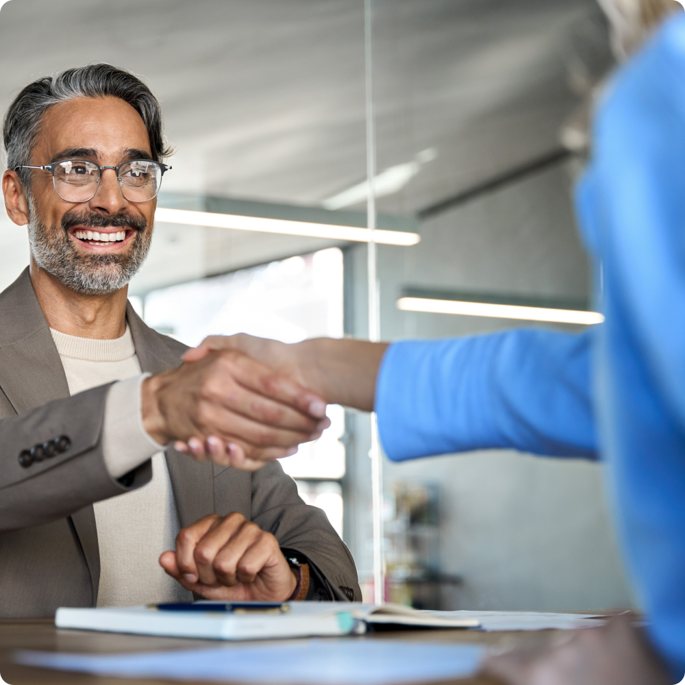 A man in a suit and glasses is shaking hands with a woman in a blue jacket.