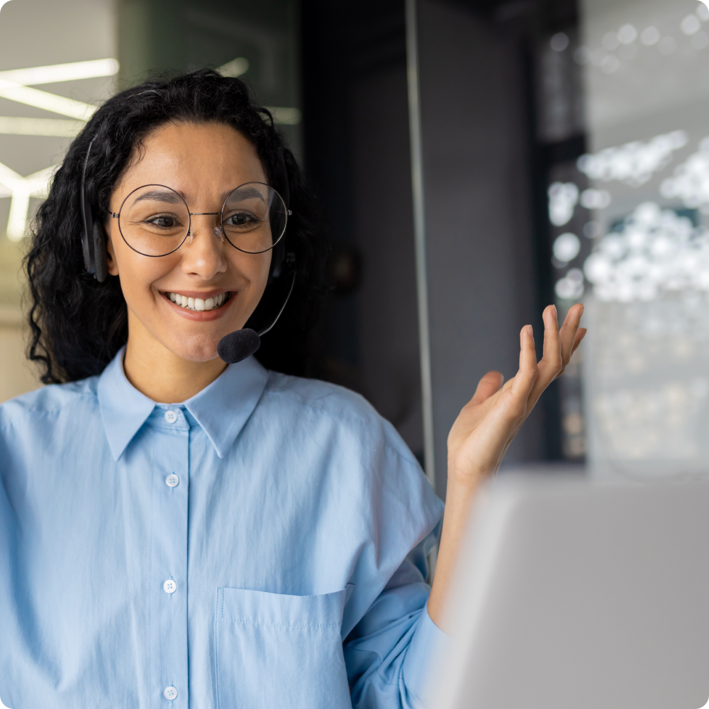 A woman wearing glasses and a headset is talking on a computer.