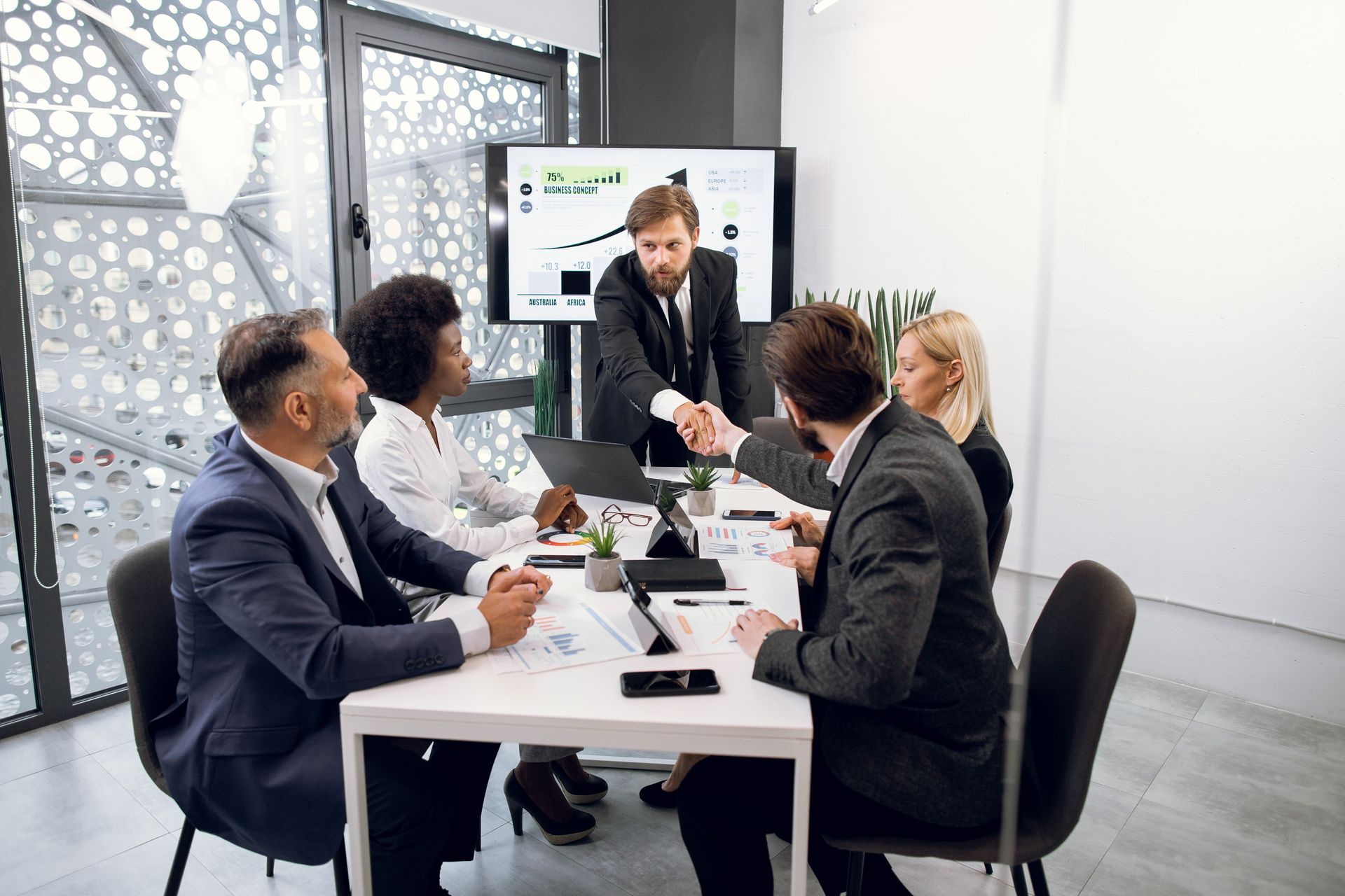 A group of business people are sitting around a table shaking hands.