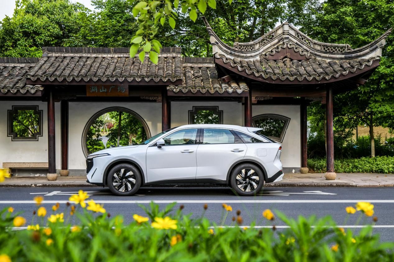 White car parked next to a traditional Chinese pavilion; flowers in the foreground.