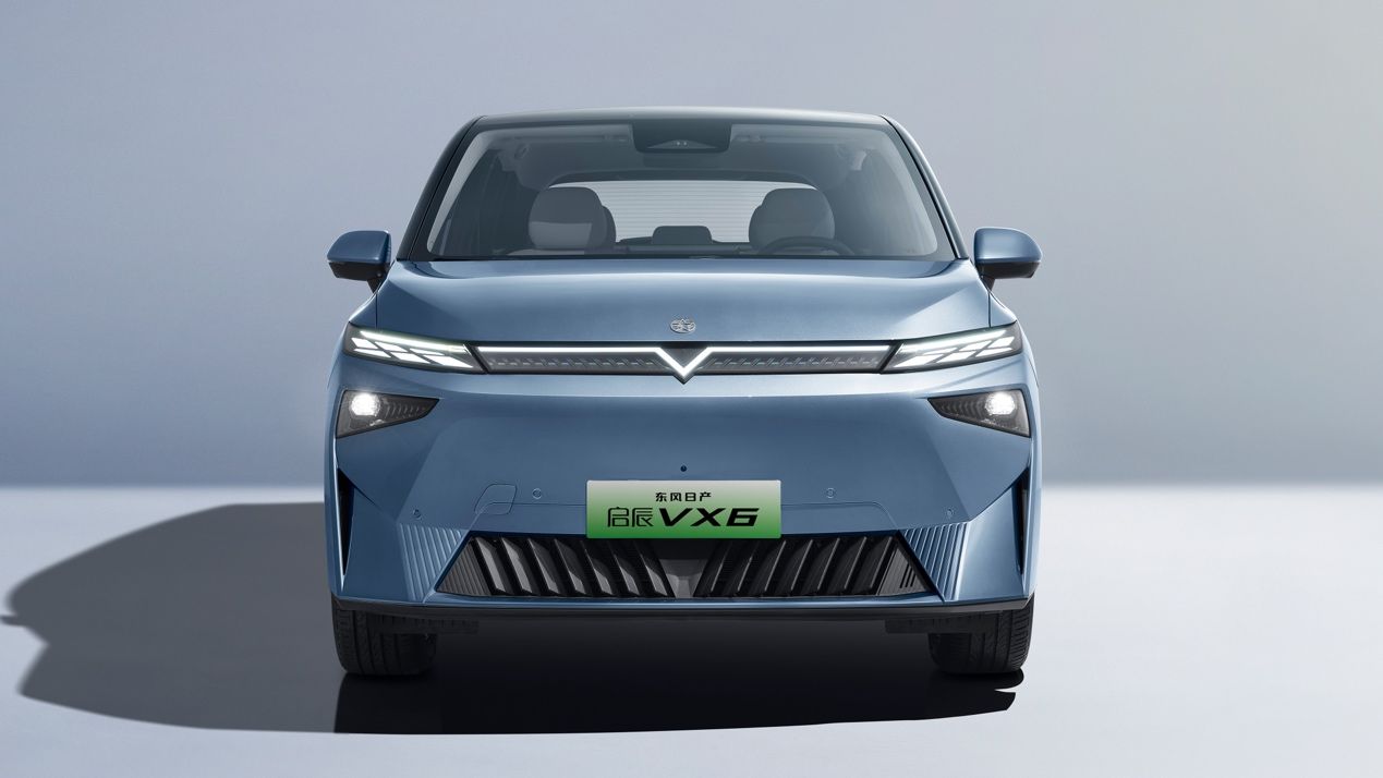 Blue electric vehicle, front view, with a central logo, and light-up elements in a studio setting.