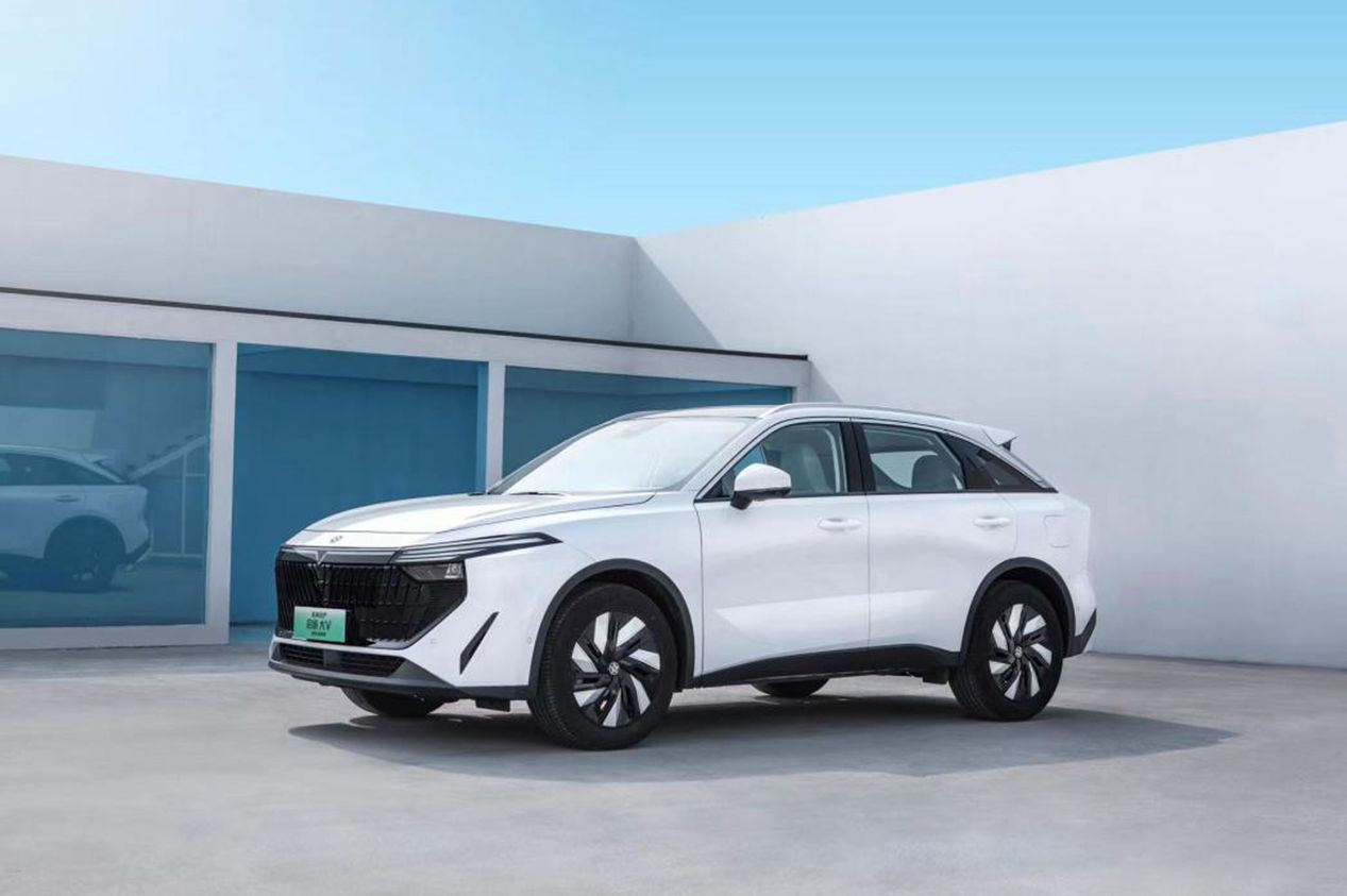White electric SUV parked outside a modern building with glass and white walls; blue sky.