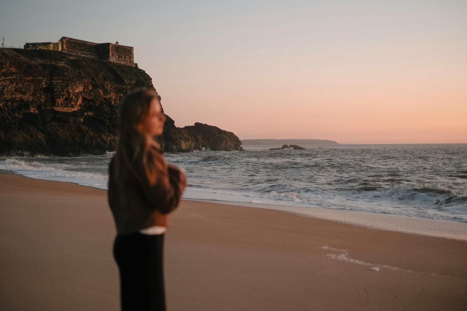 Woman standing next to a soothing ocean at sunset releasing her stored negative emotions