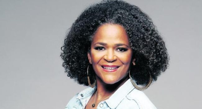 A woman with curly hair and hoop earrings is smiling for the camera.