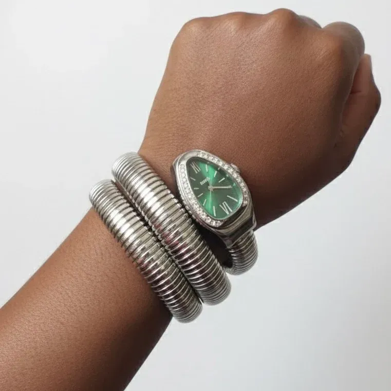 Arm wearing a silver snake-shaped watch with a green face and diamond-like border, set against a plain background.