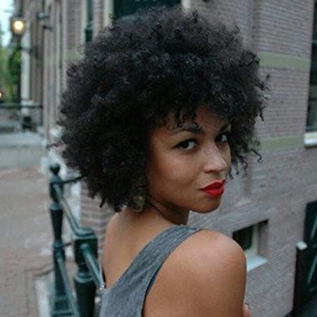 A woman with curly hair and red lipstick is standing in front of a brick building.