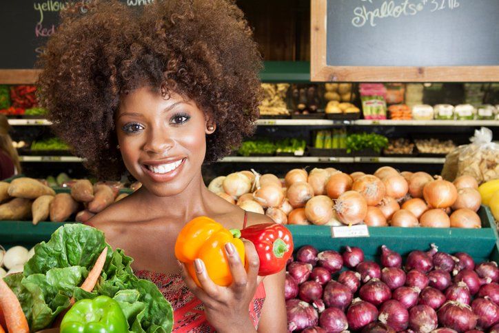 A woman is holding a pepper in a grocery store.