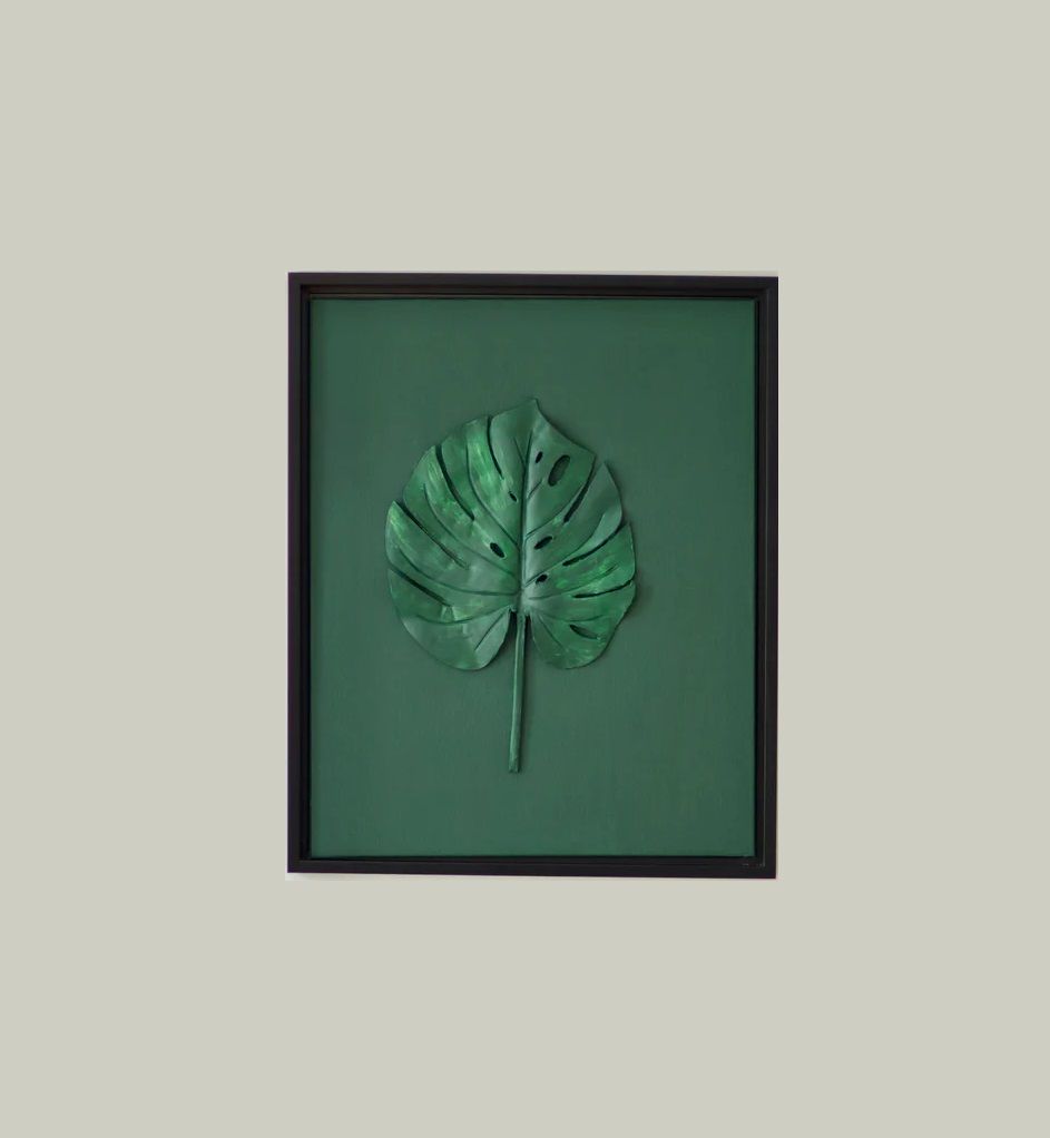 A picture of a green leaf in a black frame on a wall.