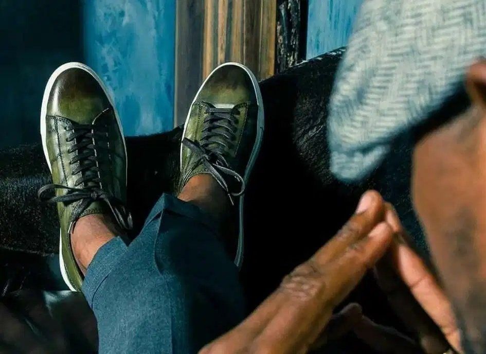 A man wearing a hat and sunglasses is sitting on a couch with his feet up.