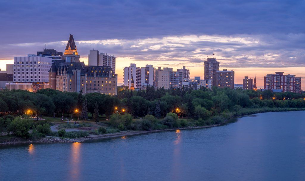 A city skyline with a lake in the foreground at sunset.