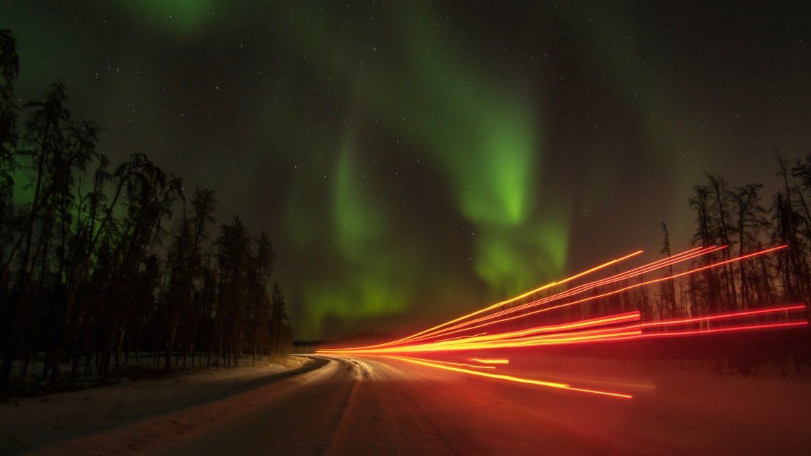 The aurora borealis is visible over a highway at night.
