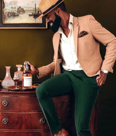 A man in a tan jacket and green pants is holding a bottle of whiskey