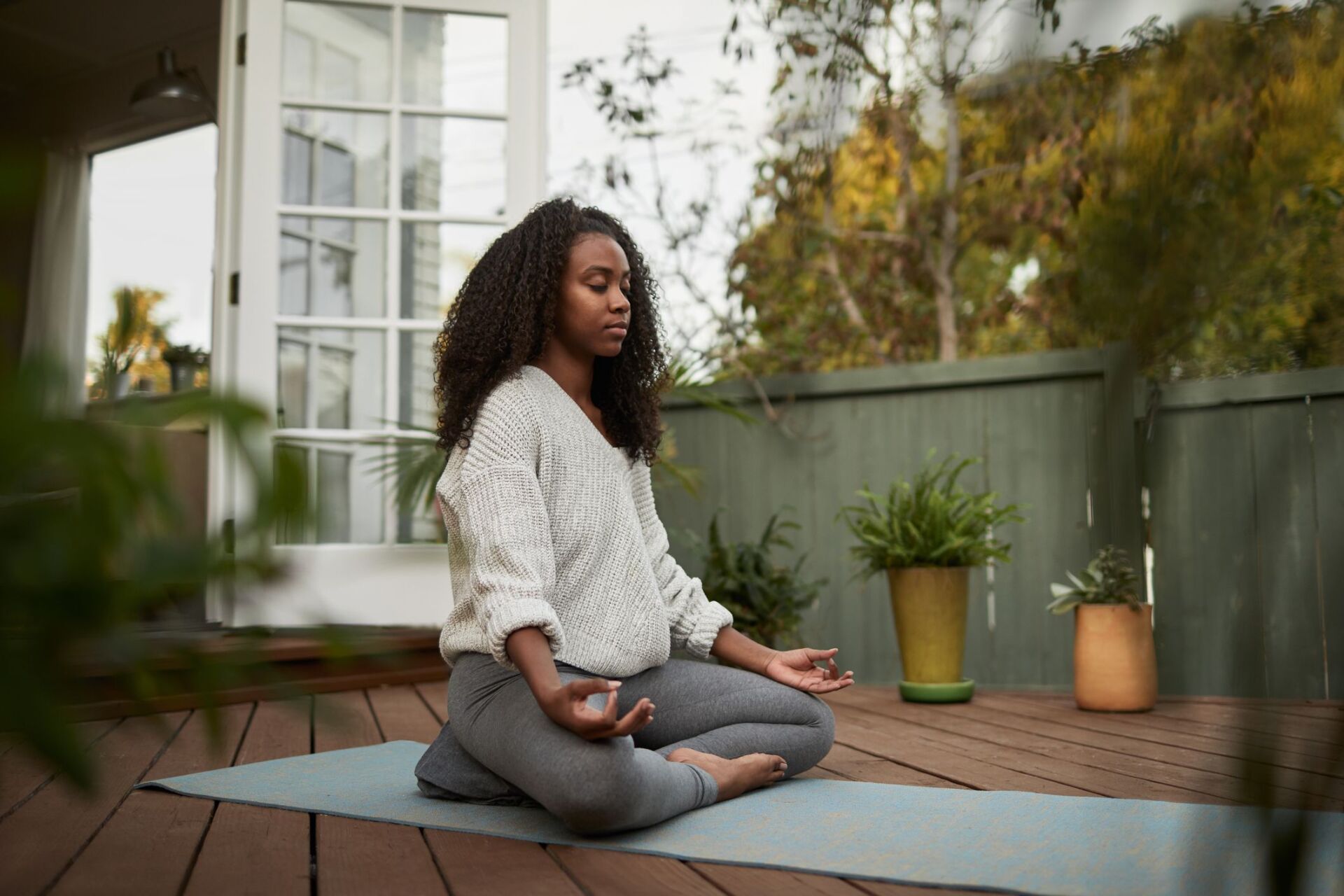 A woman is sitting on a yoga mat on a deck.