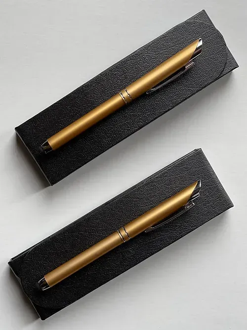 Two gold pens in black boxes on a table