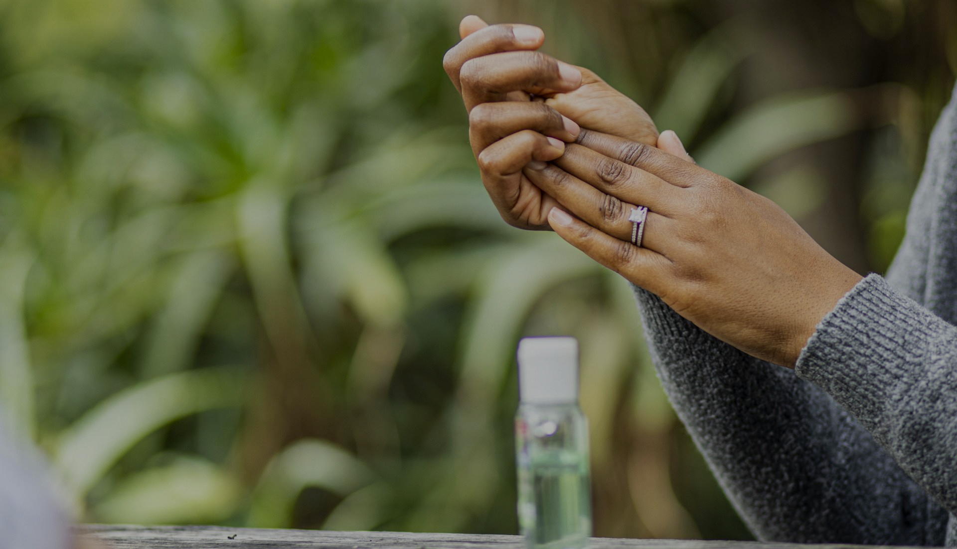 A person is washing their hands with a bottle of hand sanitizer in the background.