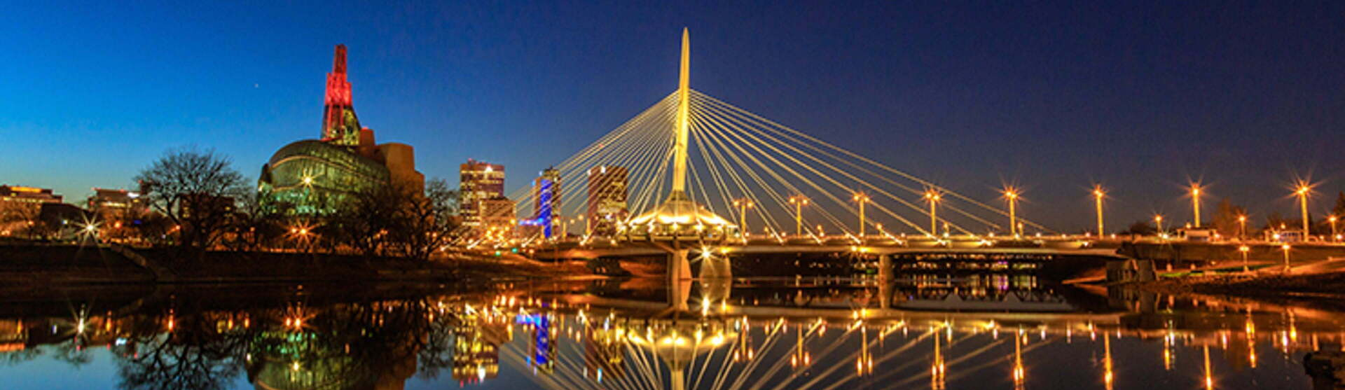A bridge over a body of water with a city in the background at night.