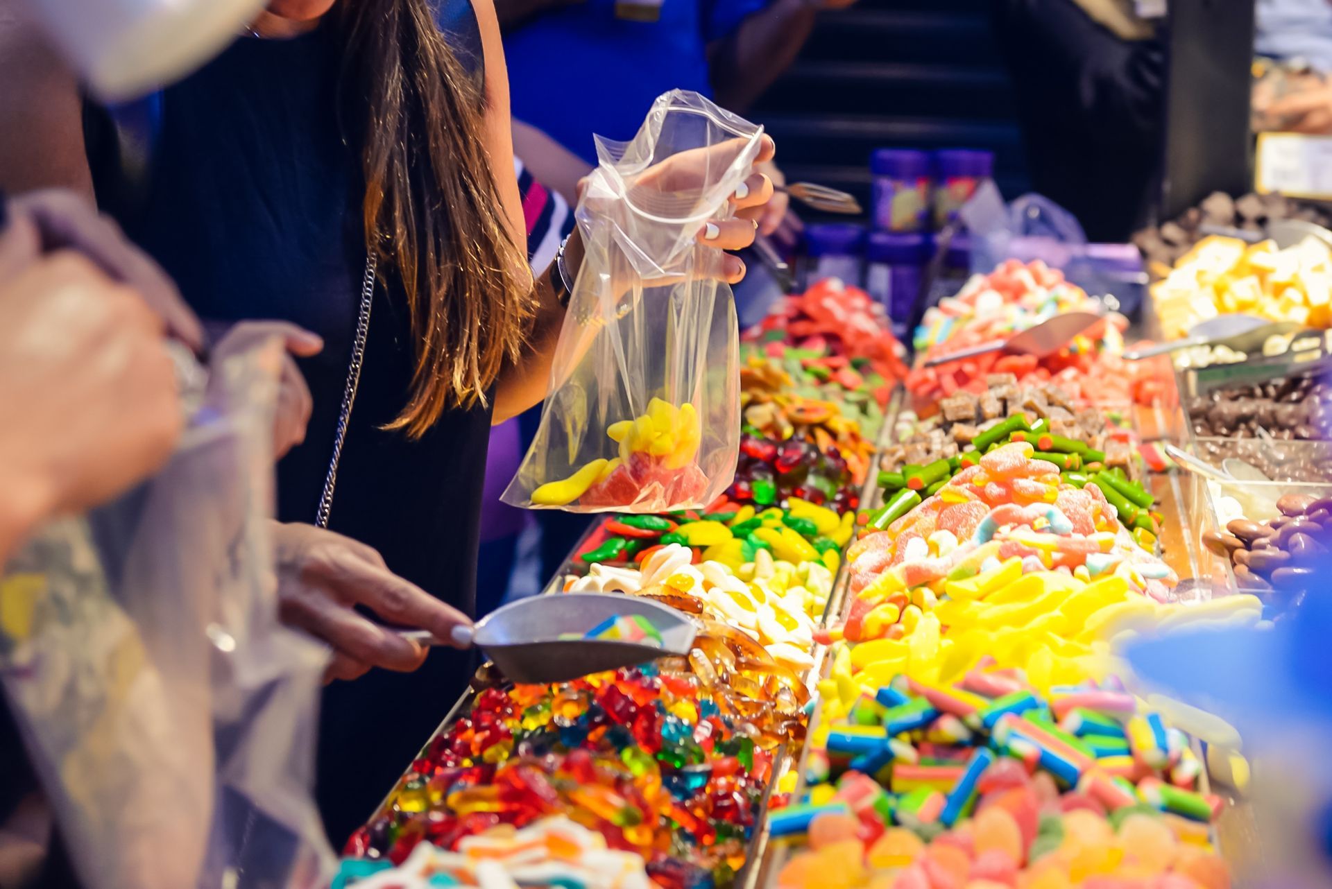 A woman is scooping candy from a bag at a candy stand.