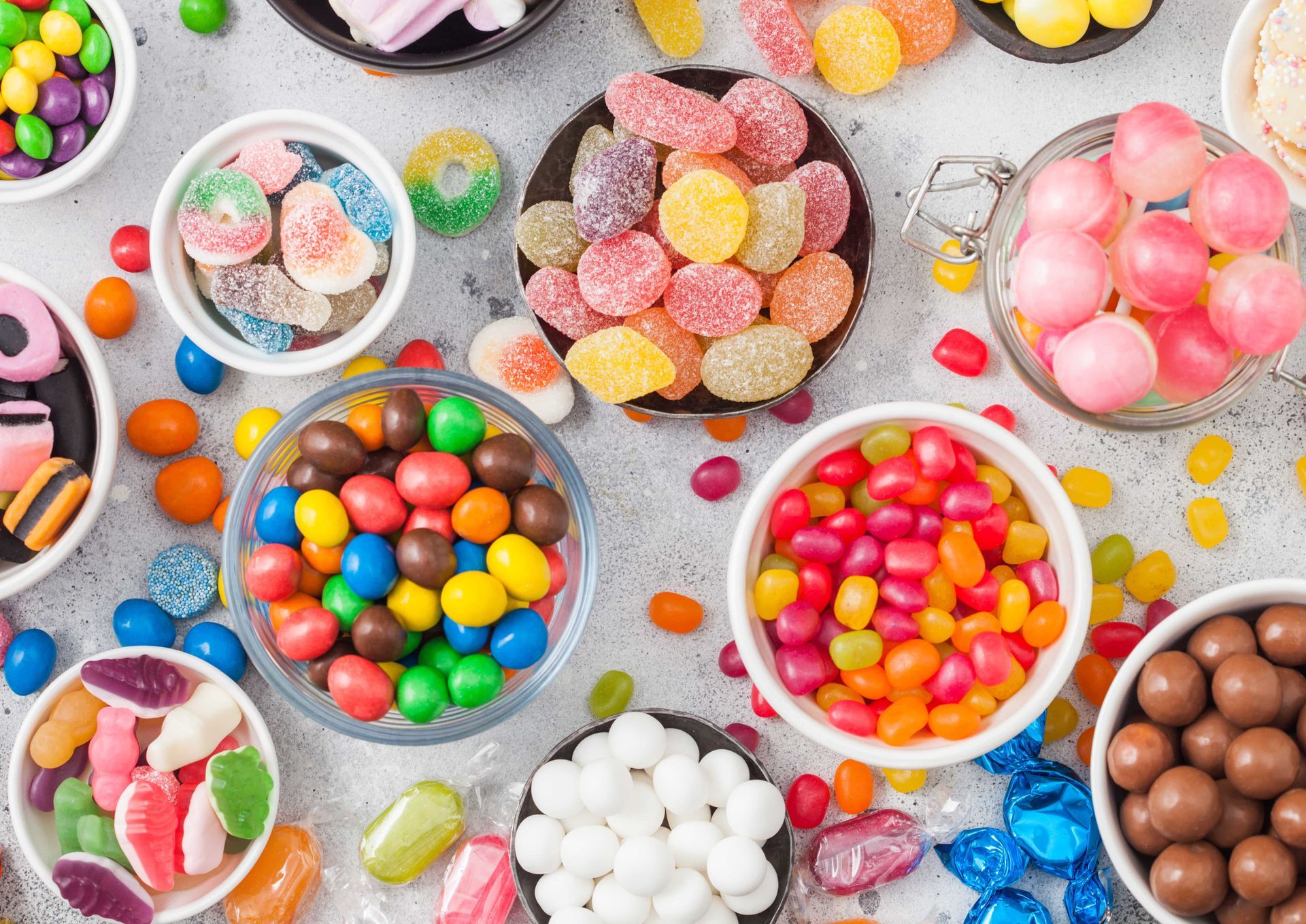 There are many different types of candy in bowls on the table.
