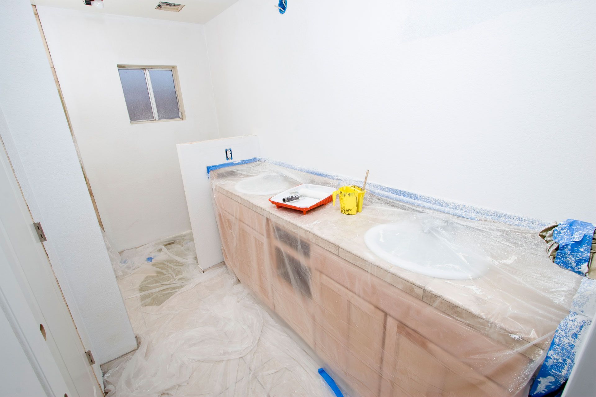 A bathroom under construction with two sinks and cabinets covered in plastic.