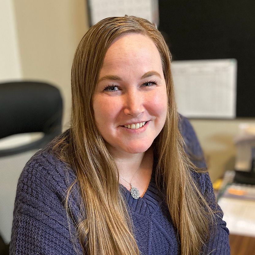 A woman in a blue sweater is smiling for the camera while sitting at a desk.