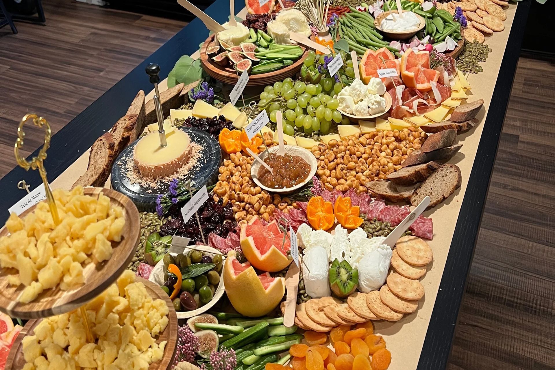 A long table with a lavish charcuterie spread: cheeses, fruits, nuts, crackers, and meats.